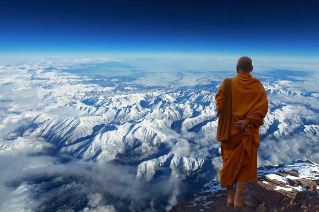 Buddhist monk on the top of a mountain looking at a snow-covered landscape below him